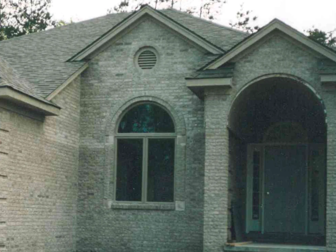 The entry of the Fraser home in 1998, an arched window under a round gable vent beside the arched porch, the pale brick showing scattered lighter units