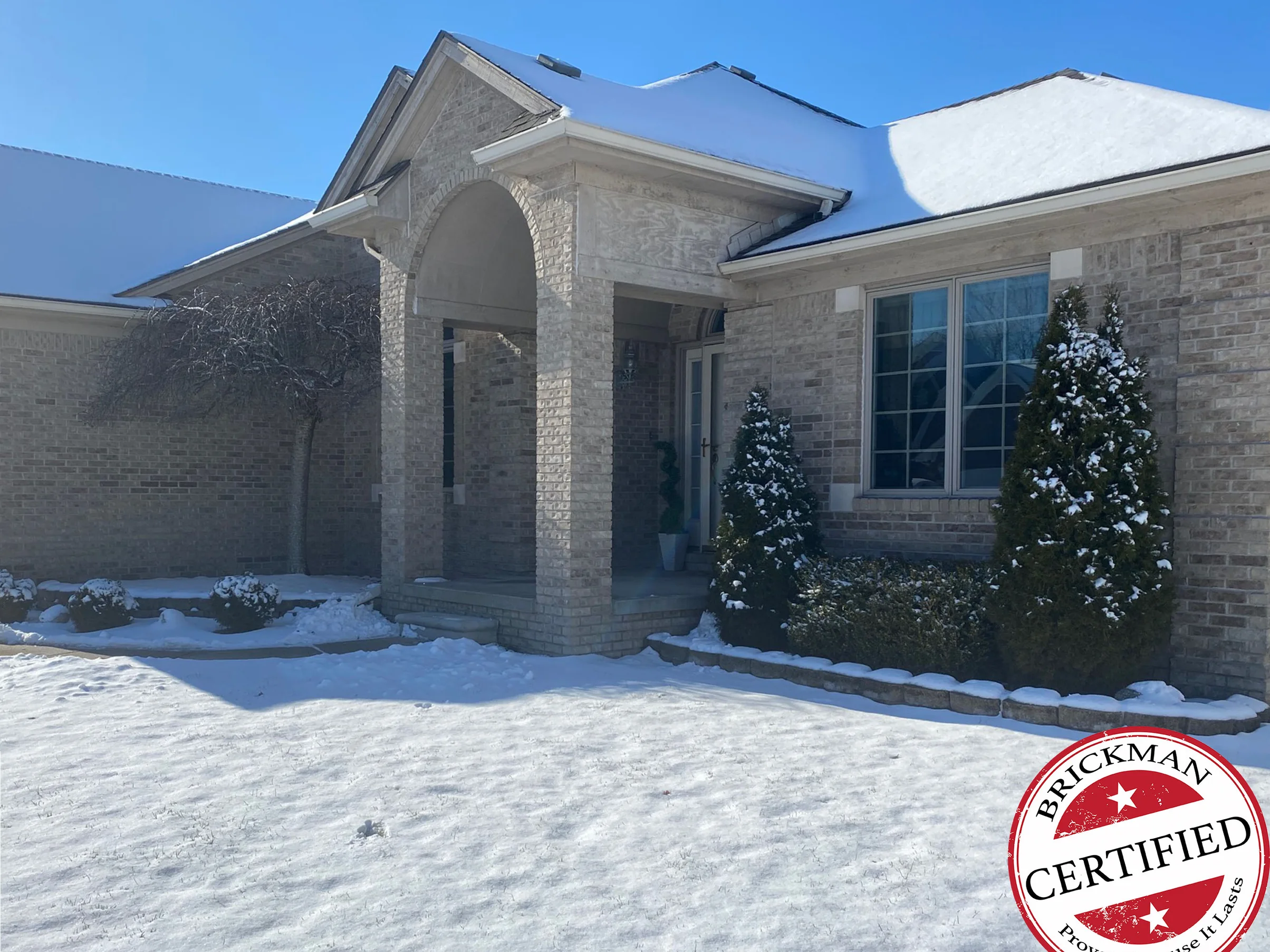 The front of the Fraser home in 2021 with snow on the ground, the entry piers, gable and side wall one buff range, with the certification stamp in the corner