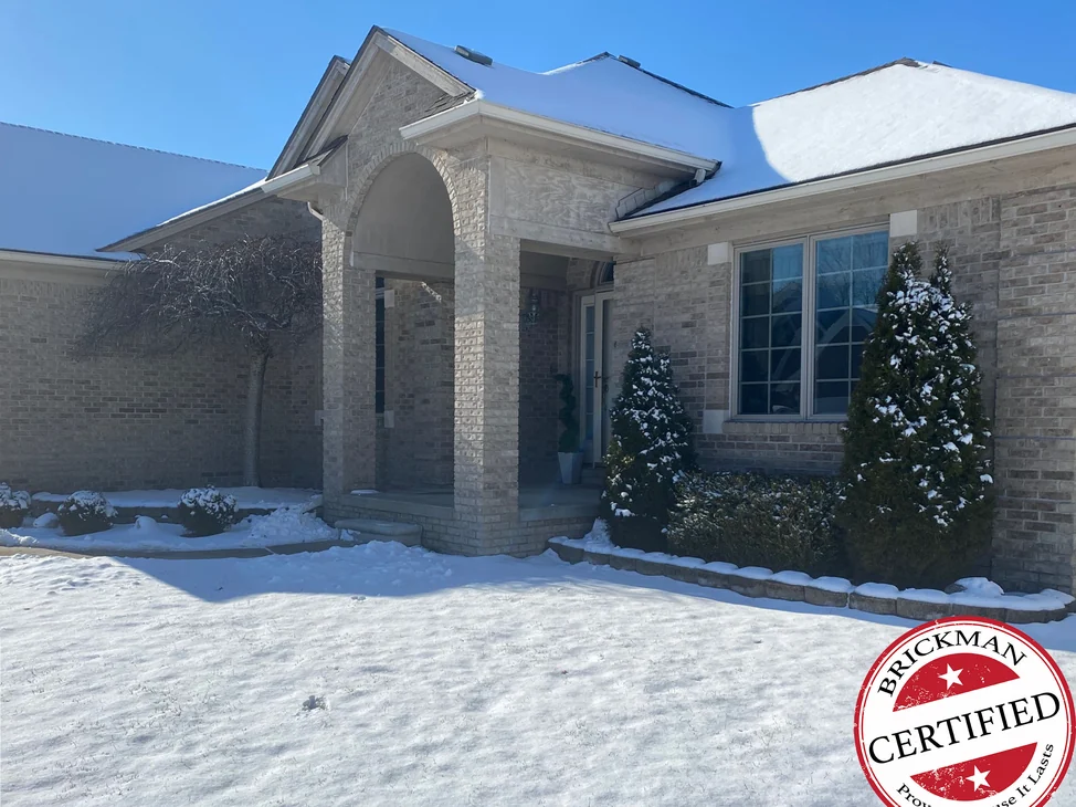 The front of the Fraser home in 2021 with snow on the ground, the entry piers, gable and side wall one buff range, with the certification stamp in the corner