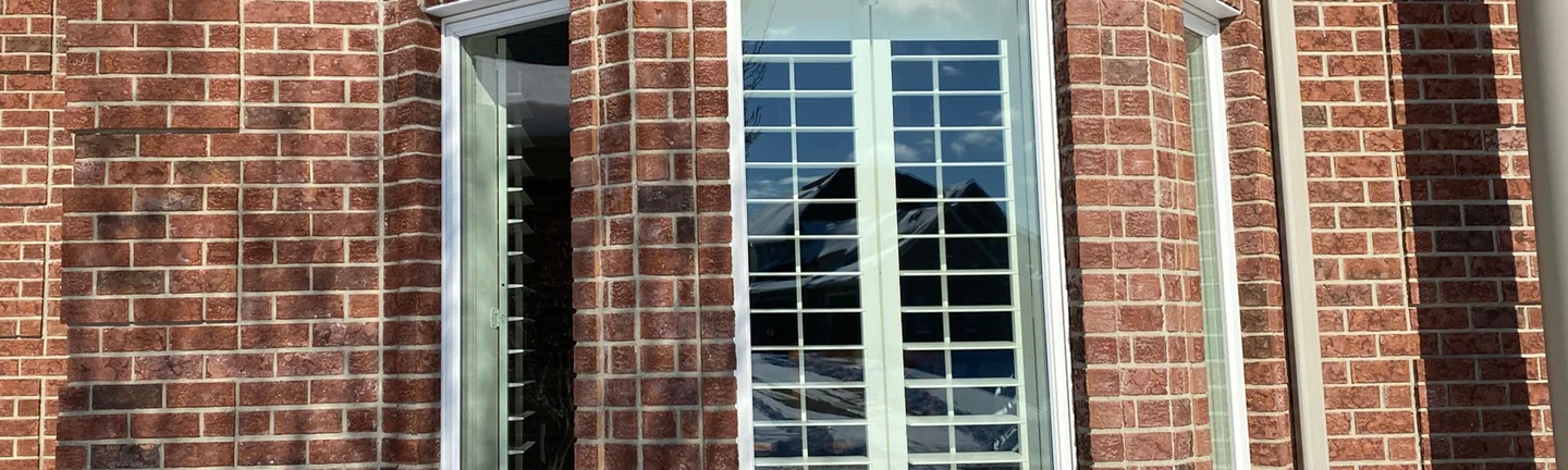 The brick bay window of the home in 2021, red brown brick reading as one range around white window frames with stone keystones above them