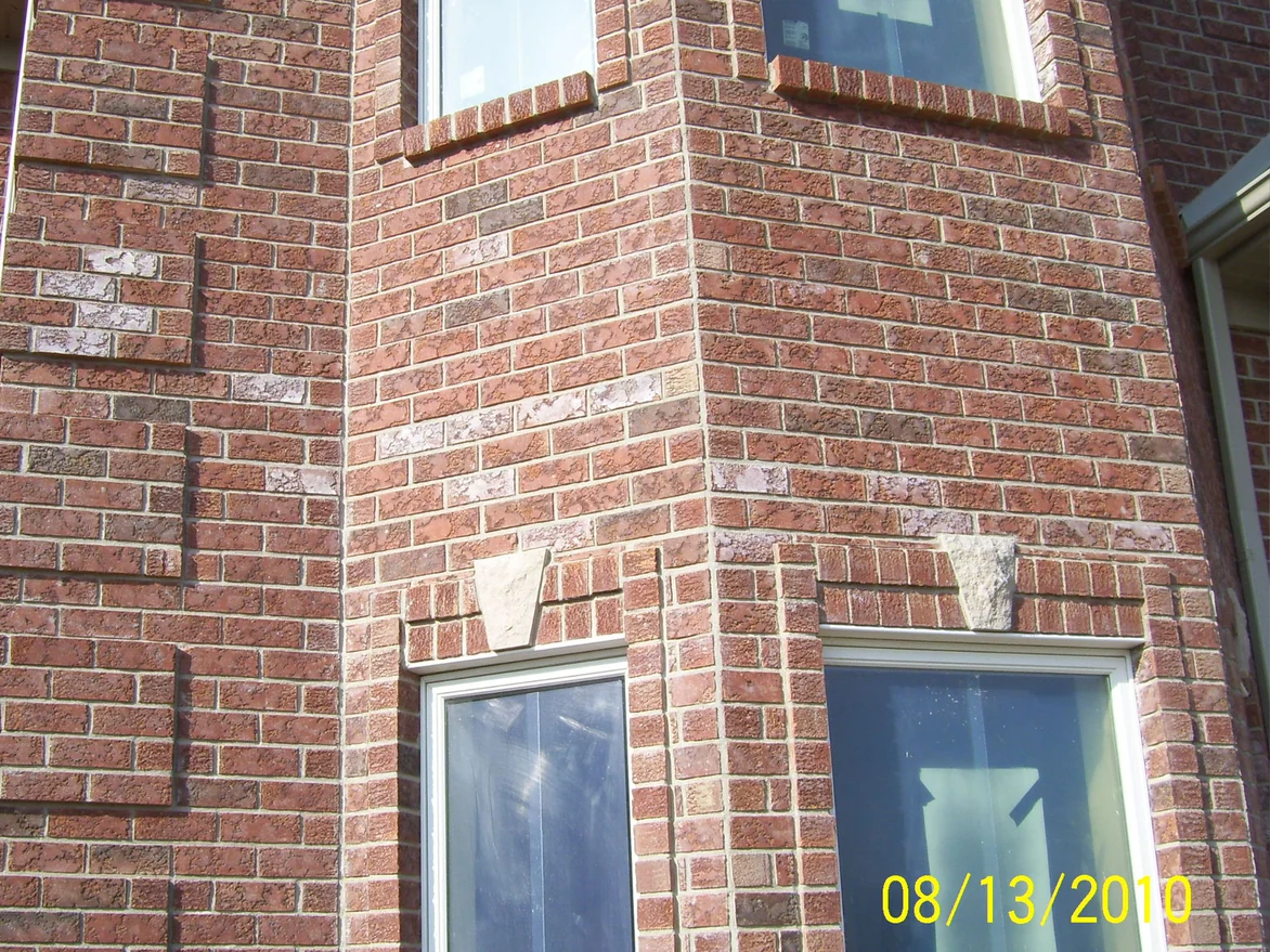 The brick bay window in August 2010 before staining, pale blotchy units scattered through the red brown wall above the stone keystones and on the flat wall beside the bay