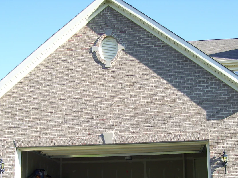 The front of the two-car garage in low evening sun on the same day in August 2007, the door open, tan grey brick from the peak and its oval vent down to the keystone over the opening