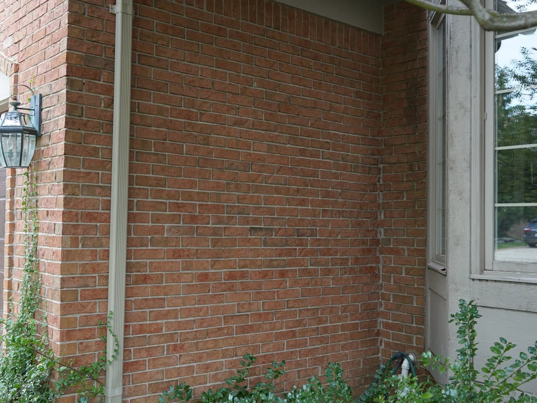 A tall panel of brick beside the bay window in 2019, evenly ranged from the eaves down to the planting