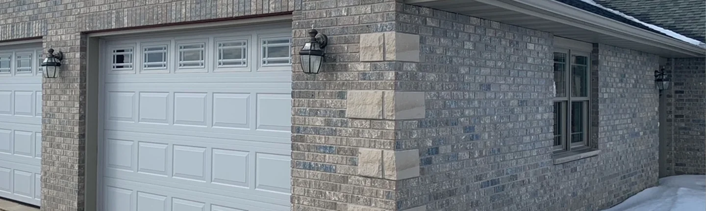 The garage corner of the Grand Mound house in 2021, grey and tan brick reading as one range across the gable and the return wall around a cut stone quoin