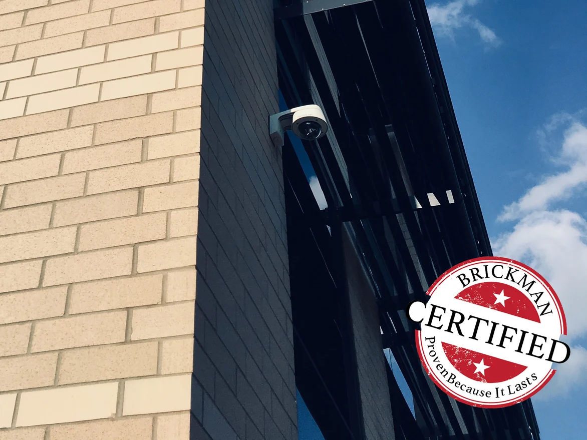 Close view of the office corner in 2019, cream brick meeting a dark return and a black metal sunshade, with the certification stamp in the frame