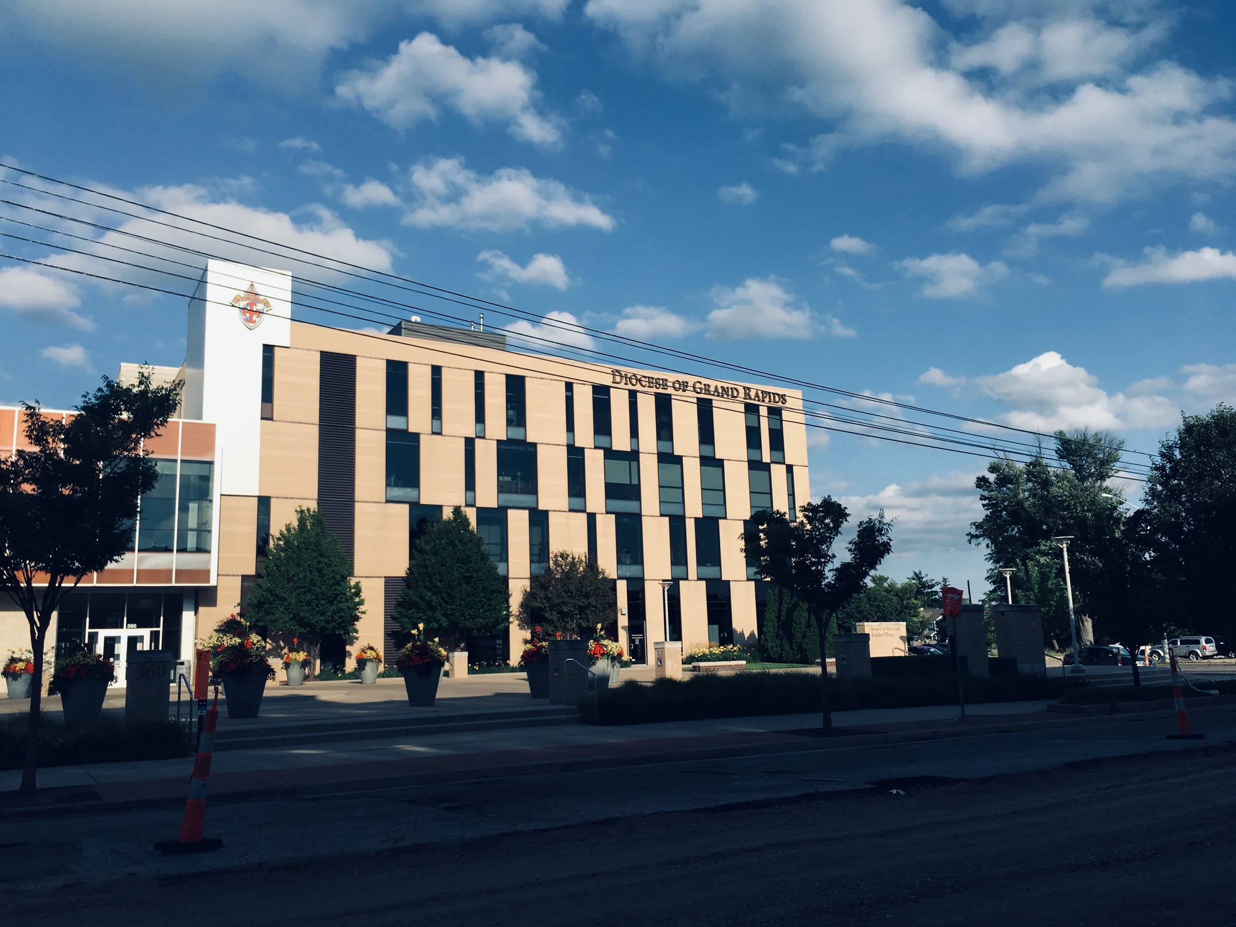 The four-story office from across the street in 2019, its cream brick running past four floors of windows under the Diocese of Grand Rapids lettering
