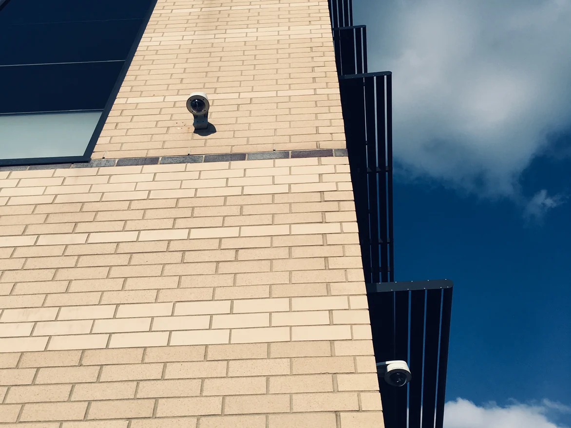 The brick wall of the office running up to its corner in 2019, the flat face in sun and the return in shadow, both in one cream and buff range