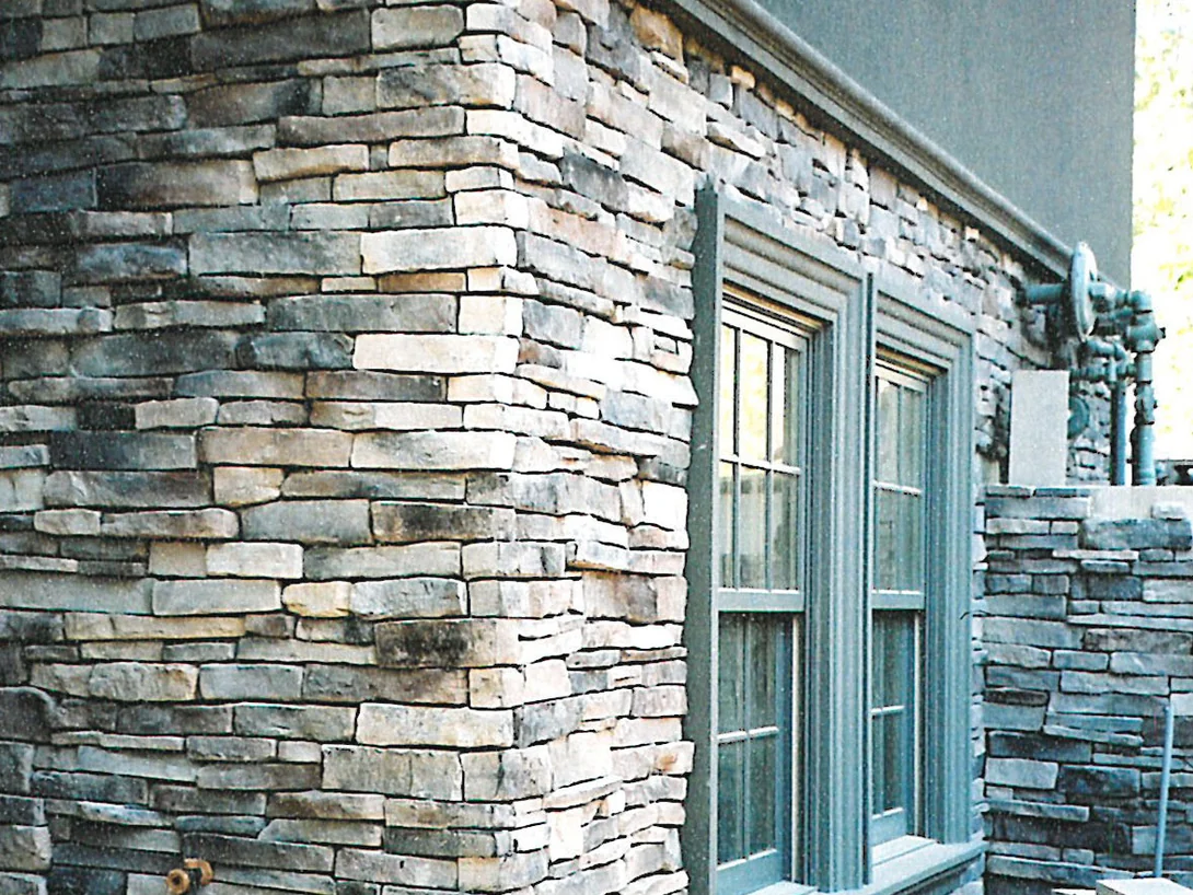 A corner of the house under construction in 2003, cream corner units turning past two windows while the wall behind them runs gray and brown