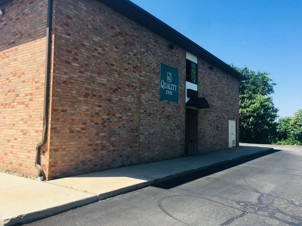 The full side wall of the hotel in 2019, two stories of red, brown and grey brick reading as one blend, with a hotel banner fixed high on it.