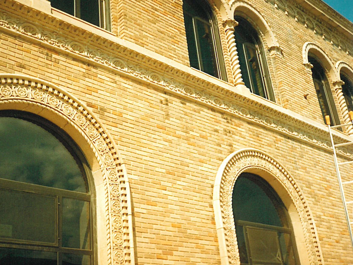 The library's upper wall before staining, its buff brick patched with darker areas between ornate arched window surrounds