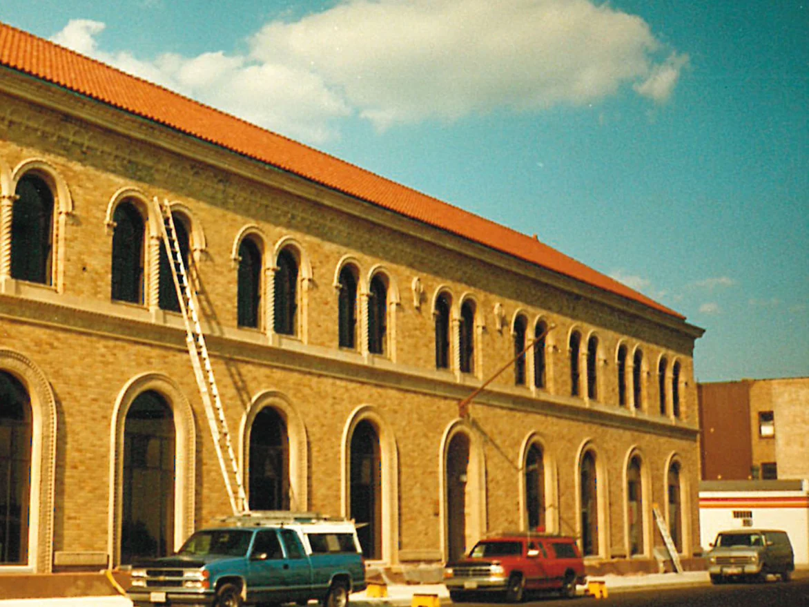 The long elevation of the library during the work, a ladder up against the second storey and work vehicles parked at the kerb