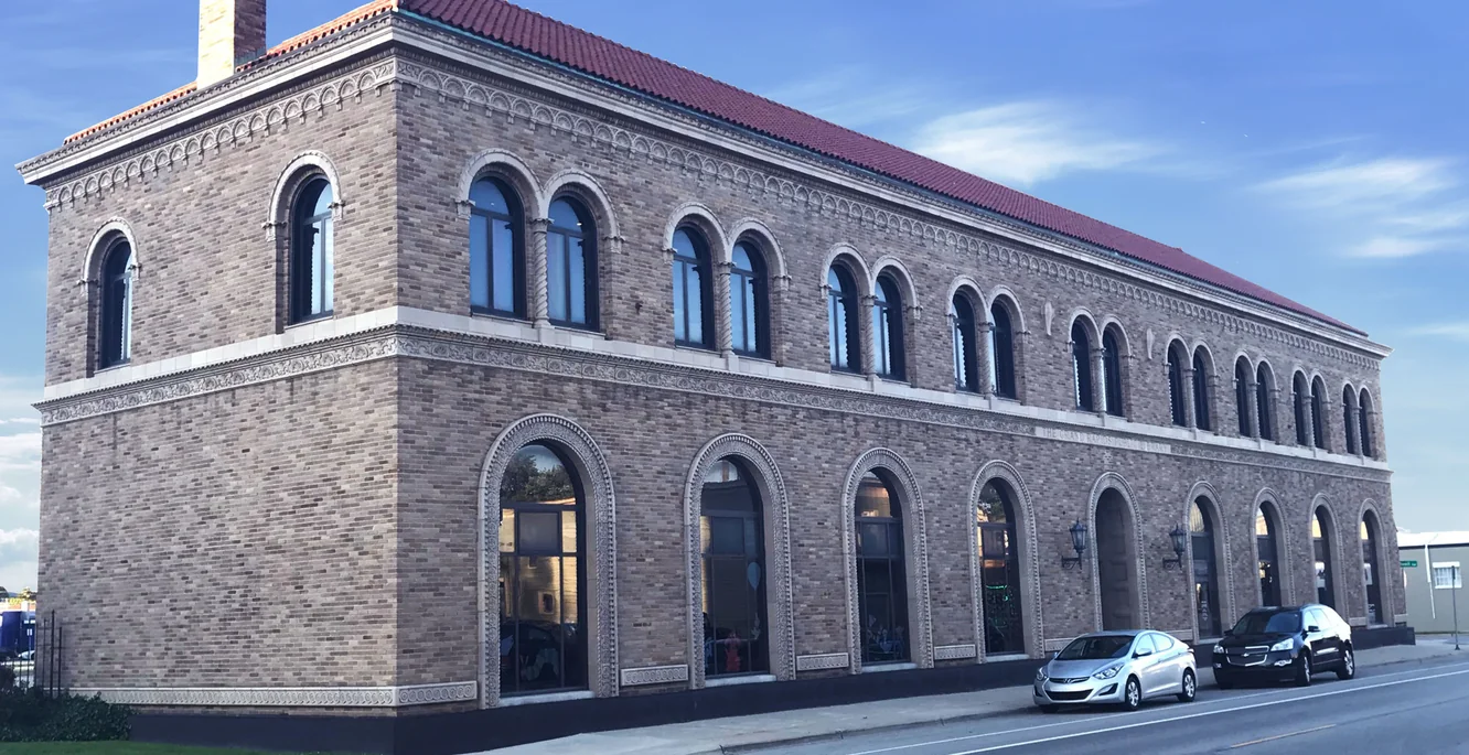 The Grand Rapids Public Library from the street, two storeys of round-arched windows in evenly blended buff brick under a clay tile roof