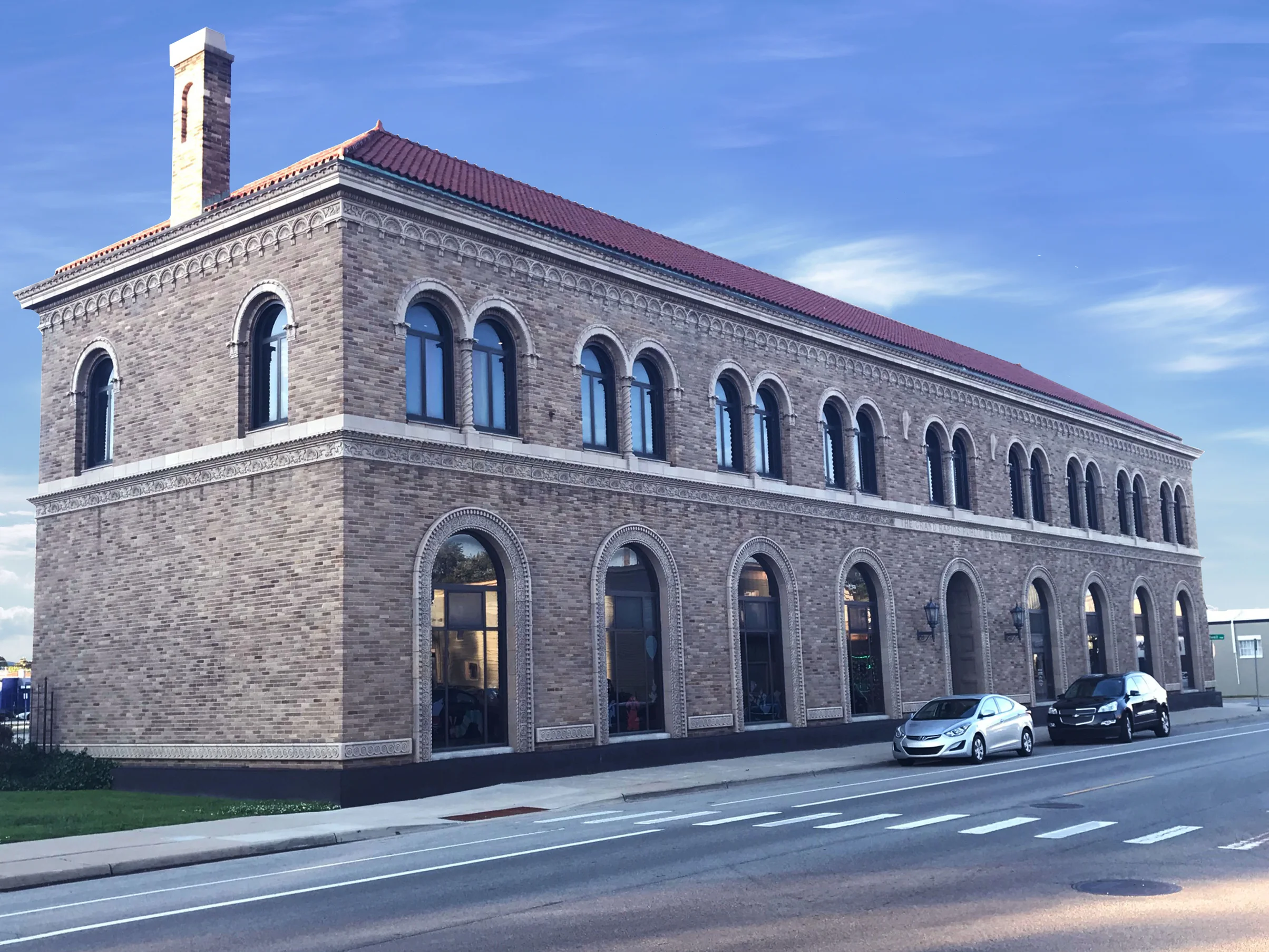 The library seen from the street corner in 2019, two storeys of evenly blended buff brick with a chimney at the near end and a clay tile roof