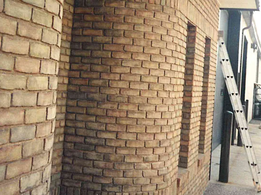 The same curved corner in 2019, seen close along the side wall with an extension ladder leaning past a narrow window, the shapes and the face brick one color
