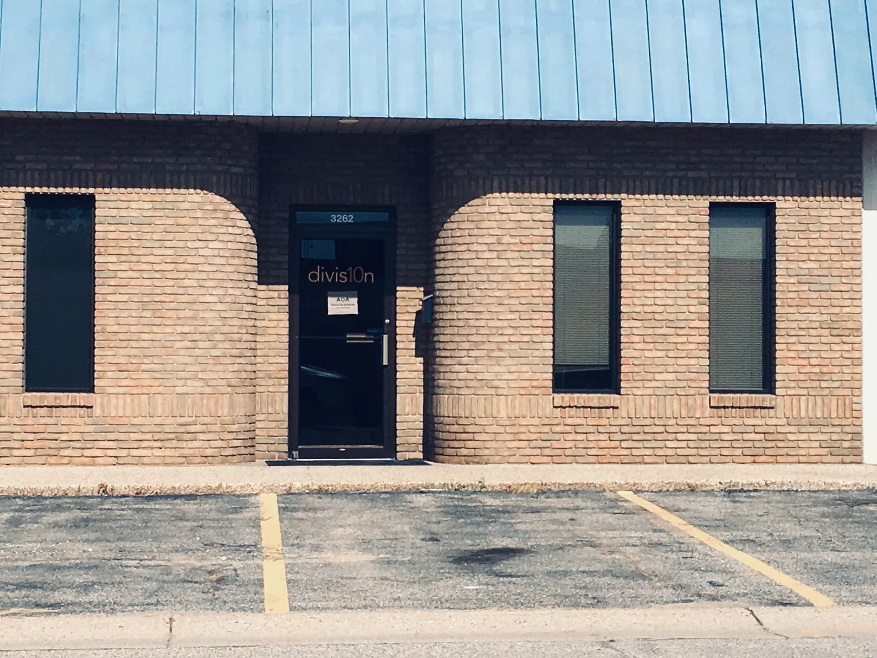 The entrance in 2019, a glass door recessed between two curved brick bays with a rowlock course at the sill line, the blue roof edge above
