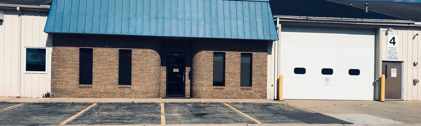 The office from across the street in 2019, tan brick with curved corners under a blue standing seam mansard roof
