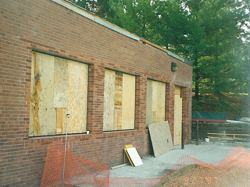 A single-story wing under construction in 1997, its window openings boarded with sheathing and orange red brick running the length of the wall