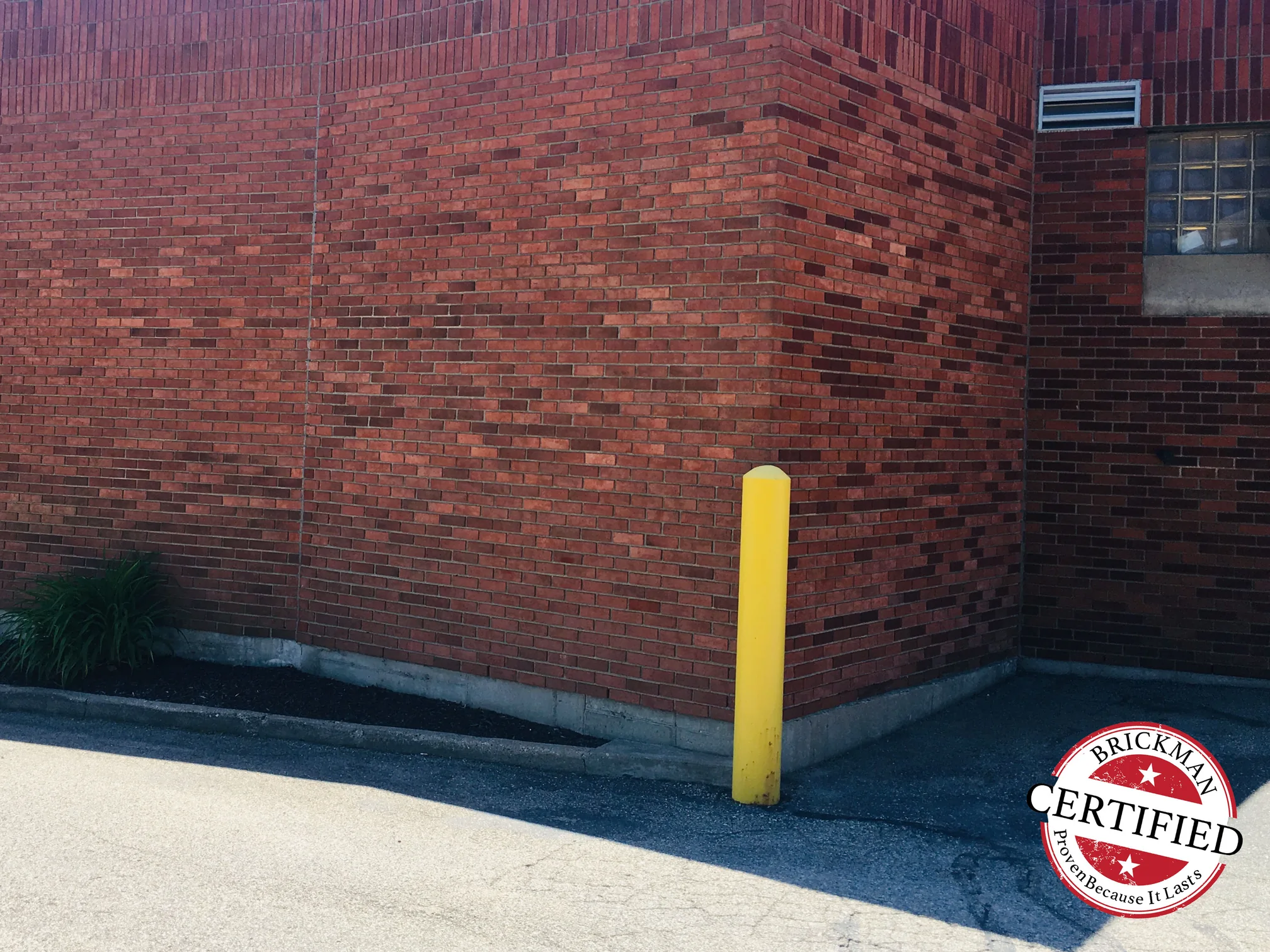 An outside corner of the store in 2019, red brick reading as one range across both faces with a yellow bollard at the base