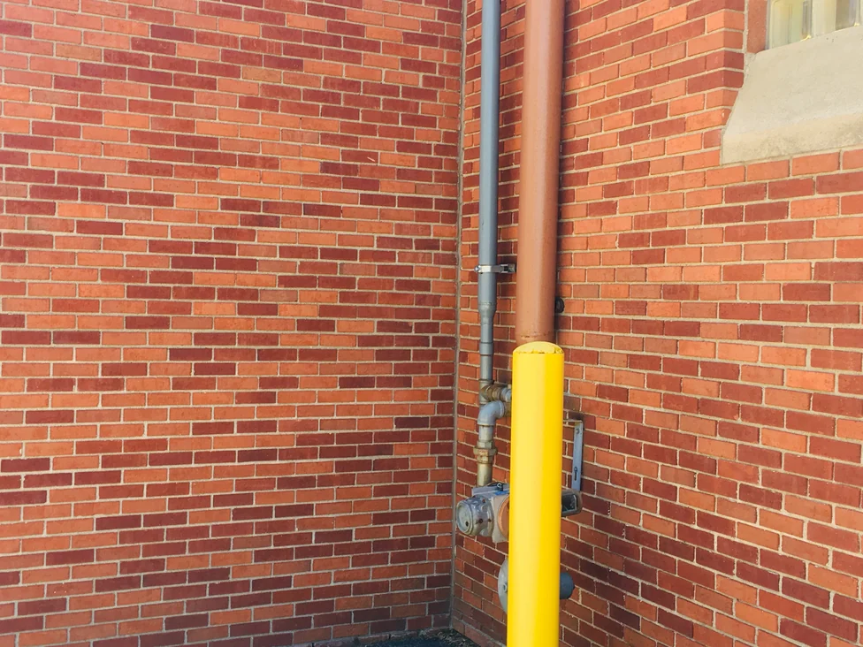 Close view of an inside corner in 2019, red and orange brick units reading as one range up to a gas riser and a yellow bollard