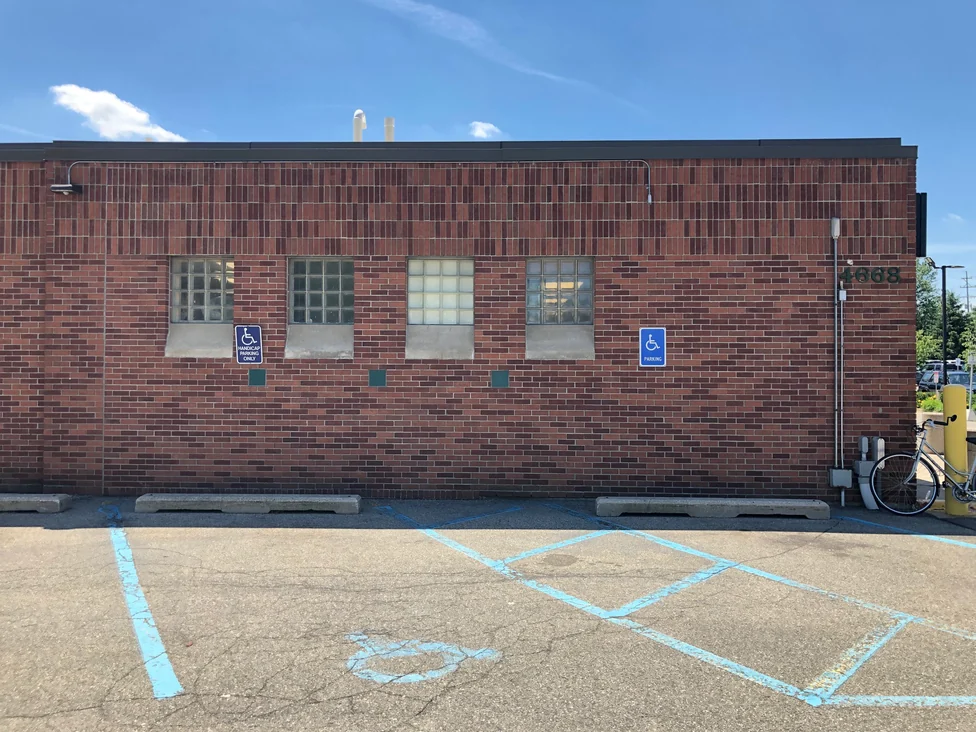 A side wall of the store in 2019, four glass block windows set in red brick under a band of upright units, above an empty parking bay