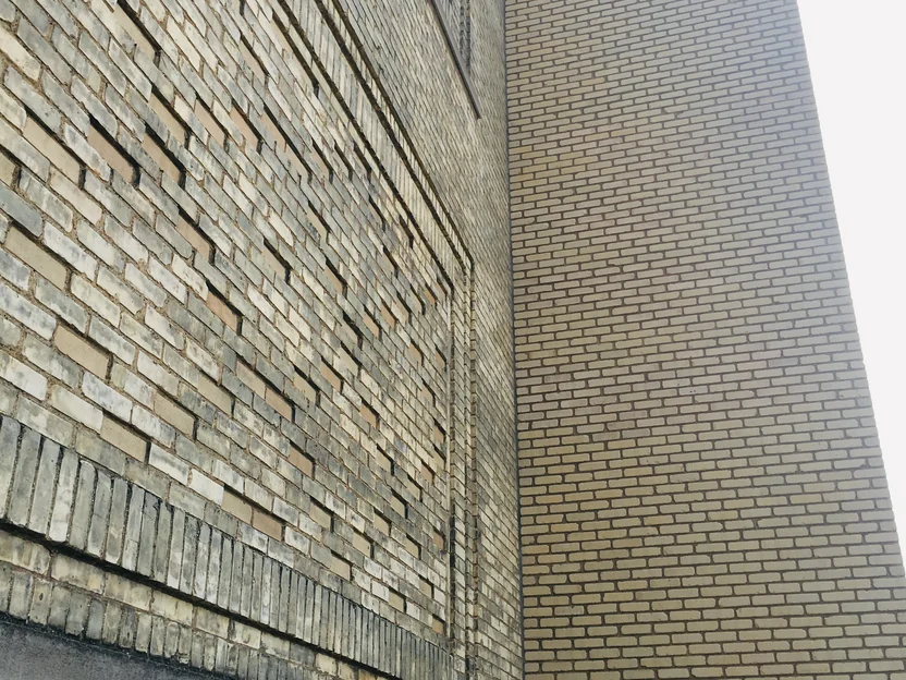Looking up the corner in 2019 where the shaft meets the original wall, patterned tan and cream brickwork at left and the uniform light brick of the shaft at right