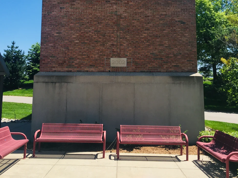 A brick column on the university campus in 2019, a 2002 date stone set in the salmon red brick above a cast stone base with three benches in front