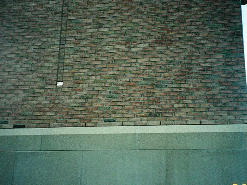 A brick wall above its cast stone base in 2002, shot in shade from a film print, the courses reading darker red and brown with a vertical joint line running down the left
