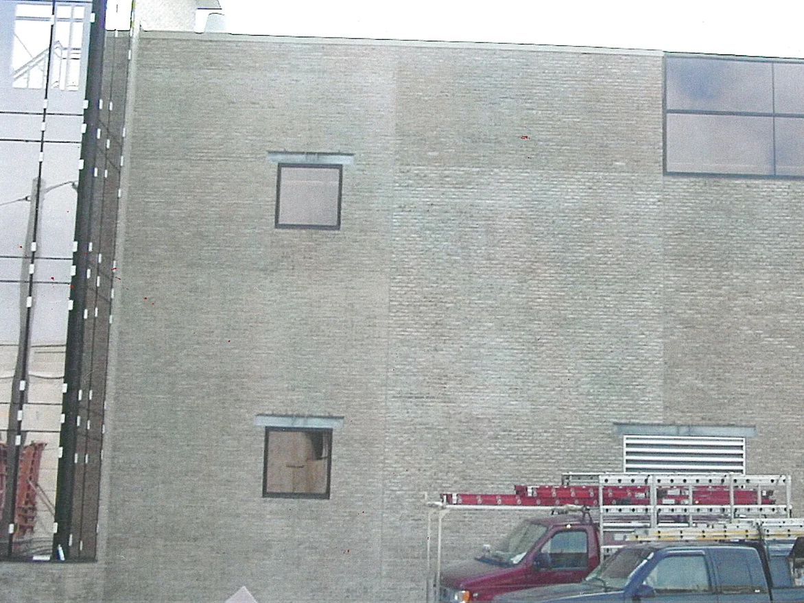 The blank end wall of the building in 2000, its brick a flat pale grey buff around two stacked square windows and a louvre vent, with two Masonry Cosmetics trucks parked at the base