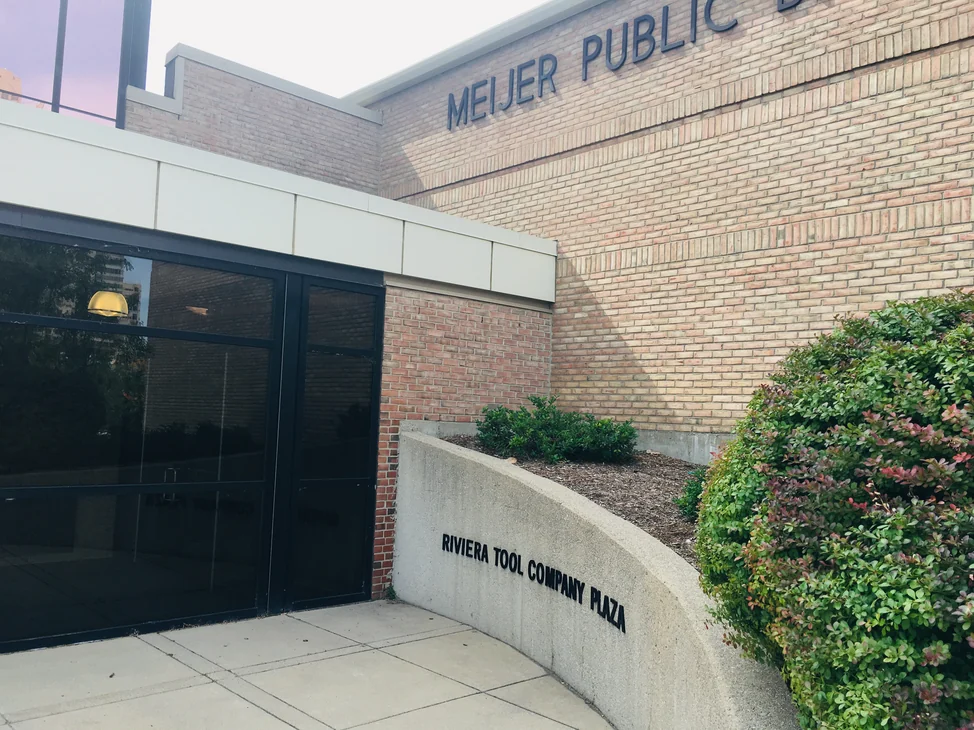 The entrance to the Meijer Public Broadcast Center in 2019, buff brick carrying the building lettering above the canopy and a lower band of red brick beside the doors.