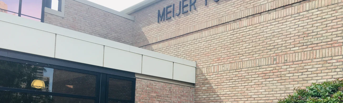 Buff brick carrying the lettering of the Meijer Public Broadcast Center in 2019, above the entrance canopy