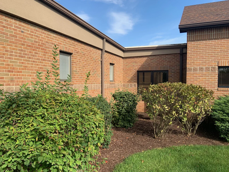 An inside corner of the building in 2019 where two wings meet, brick above a continuous band of split faced block, with clipped shrubs and mulch beds along the base.