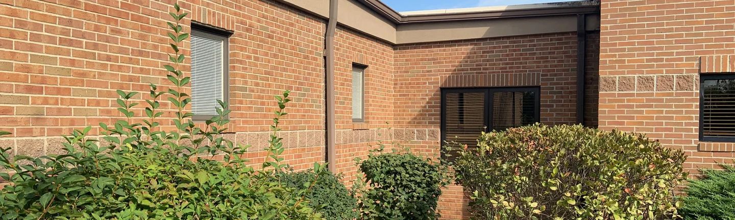 An inside corner of the Granger medical building in 2019, brick above a band of split faced block, with clipped shrubs along the wall
