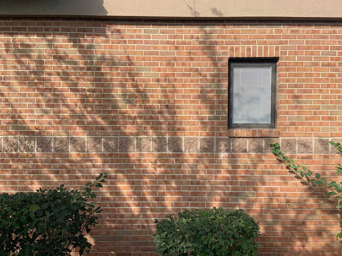 A flat stretch of wall in 2019 with one blinded window, the split faced block course carrying straight through below the sill and the brick above and below it holding the same range