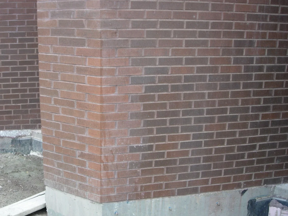 An outside corner of the library in 2007, the shaped units turning the corner reading pale orange against the darker red brown brick on both walls, the ground still bare at the base