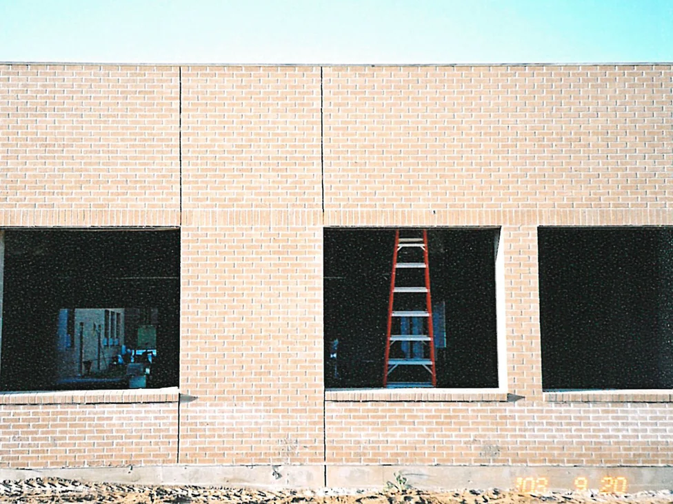 The new addition in 2003 before staining, pale cream brick running past three unglazed window openings above bare graded ground