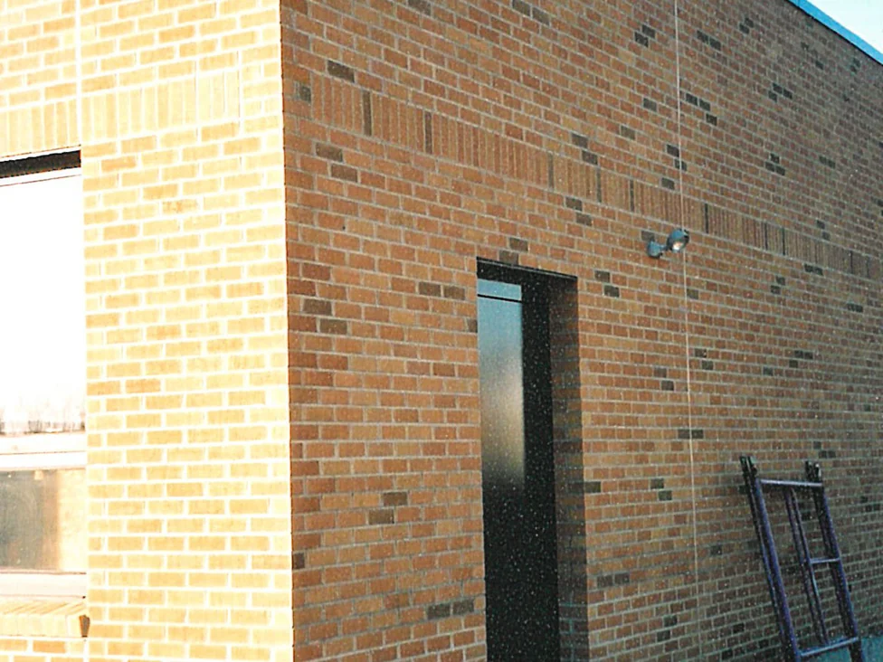 An outside corner of the addition partway through, the long wall carrying a red and tan blend with darker units through it while the return beside it is still pale cream