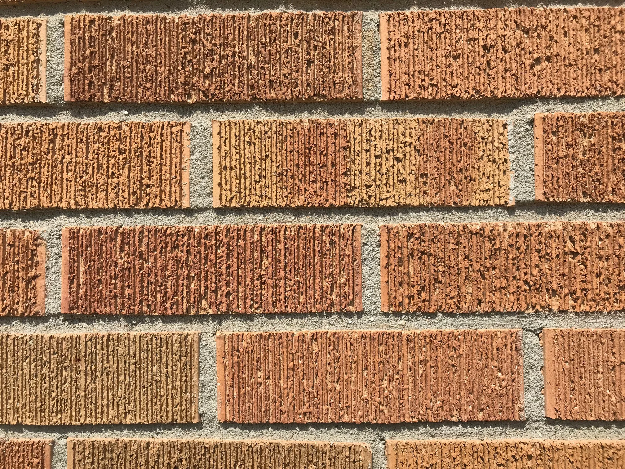 Close view of the stained brick at unit scale in 2019, wire-cut faces running from orange through red to tan between grey mortar joints
