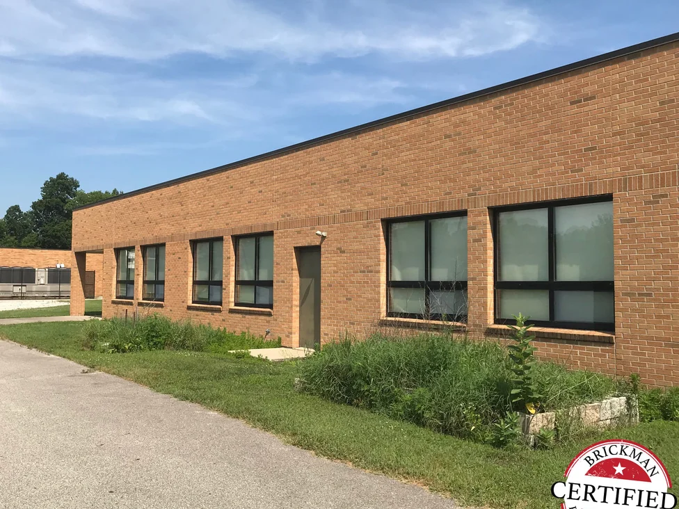 The long elevation seen down the drive in 2019, the brick holding one red and tan range past every window, the frame carrying the Brickman Certified stamp