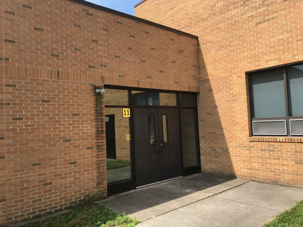 A recessed side entrance in 2019 with a numbered door plate, the brick of the two walls meeting at the doorway reading in the same red and tan range