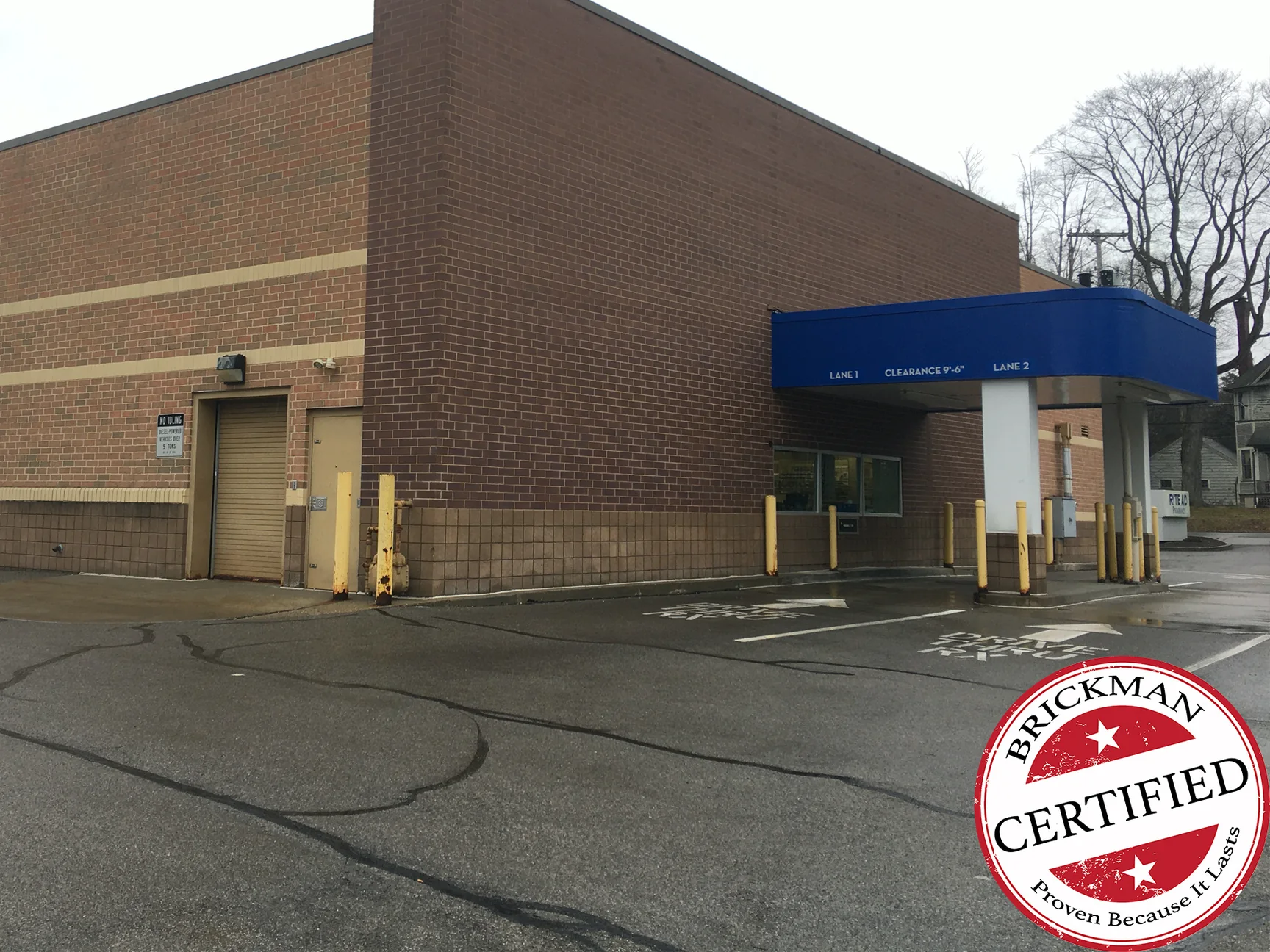 The side elevation of the Rite Aid in 2020 from the parking lot, the corrected wall at the drive-thru corner one dark brown above the block base, with the certification stamp in the corner