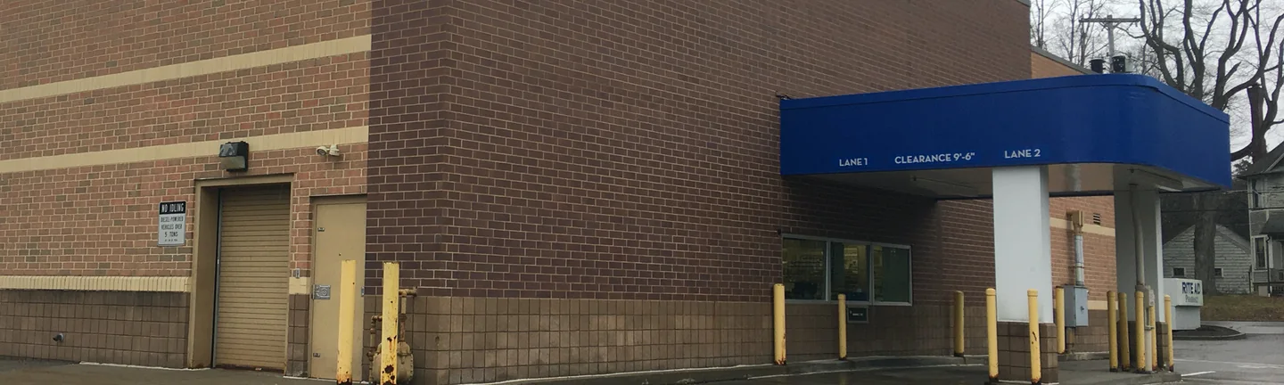 The drive-thru wall of the Rite Aid in Greenville in 2020, dark brown brick above a block base with the blue canopy at the corner