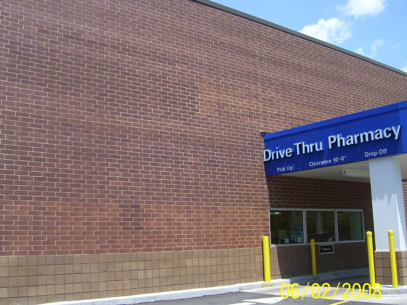 The drive-thru pharmacy wall in June 2008 before staining, dark brown brick with lighter tan units scattered across the whole face under a blue Drive Thru Pharmacy canopy sign