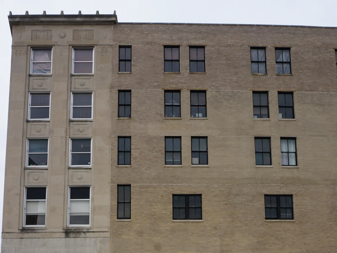 The corner of the building in 2019 from the parapet down, the cast stone tower on the left and four stories of stained brick running away from it