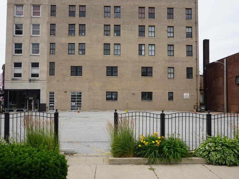 The building in 2019 from across its parking lot, its main wall and limestone corner tower reading as one buff range.