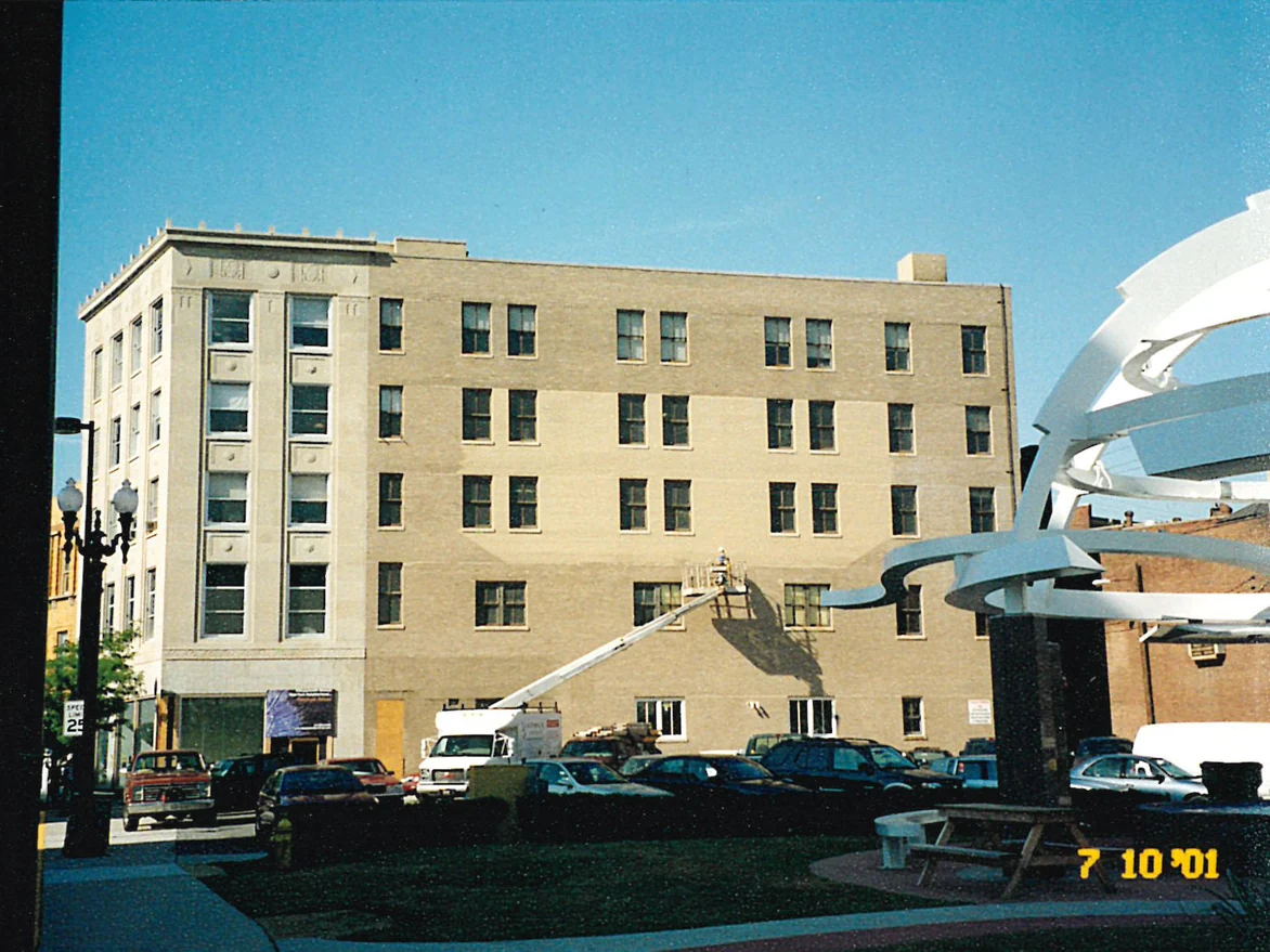 The building from across the street in 2001, five stories of buff brick with a boom lift raised to an applicator working the main wall