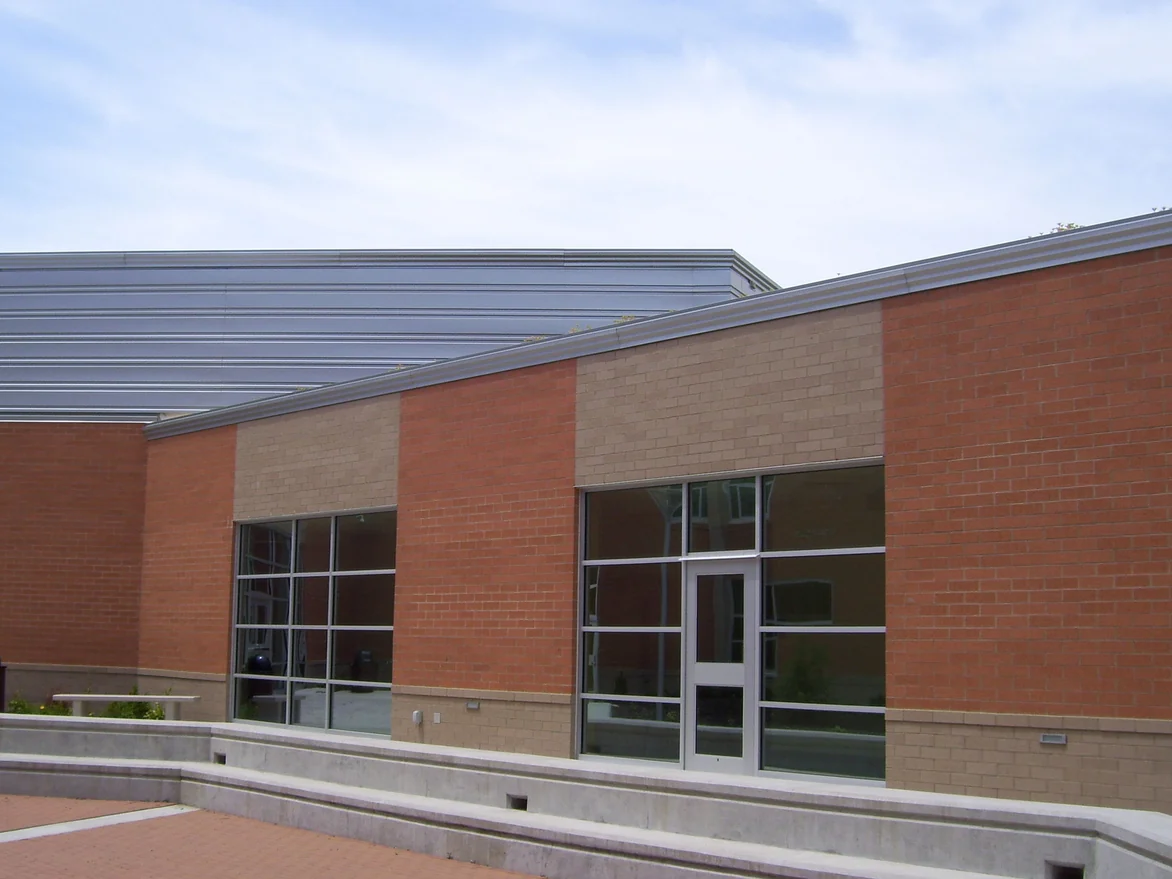 The courtyard elevation in 2011 after staining, two window bays each topped by a panel of tan brick between piers of orange brick, with a metal roof behind and a concrete planter wall in front