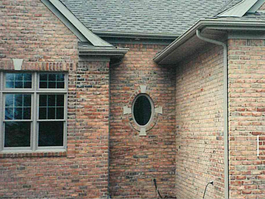 An inside corner of the house in 2000, an oval window with a cast stone surround between a double-hung window and a return wall, under grey shingles