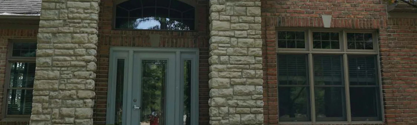 The front entry of the Highland house in 2019, a split-face stone arch and piers with red brick walls and a window to the right