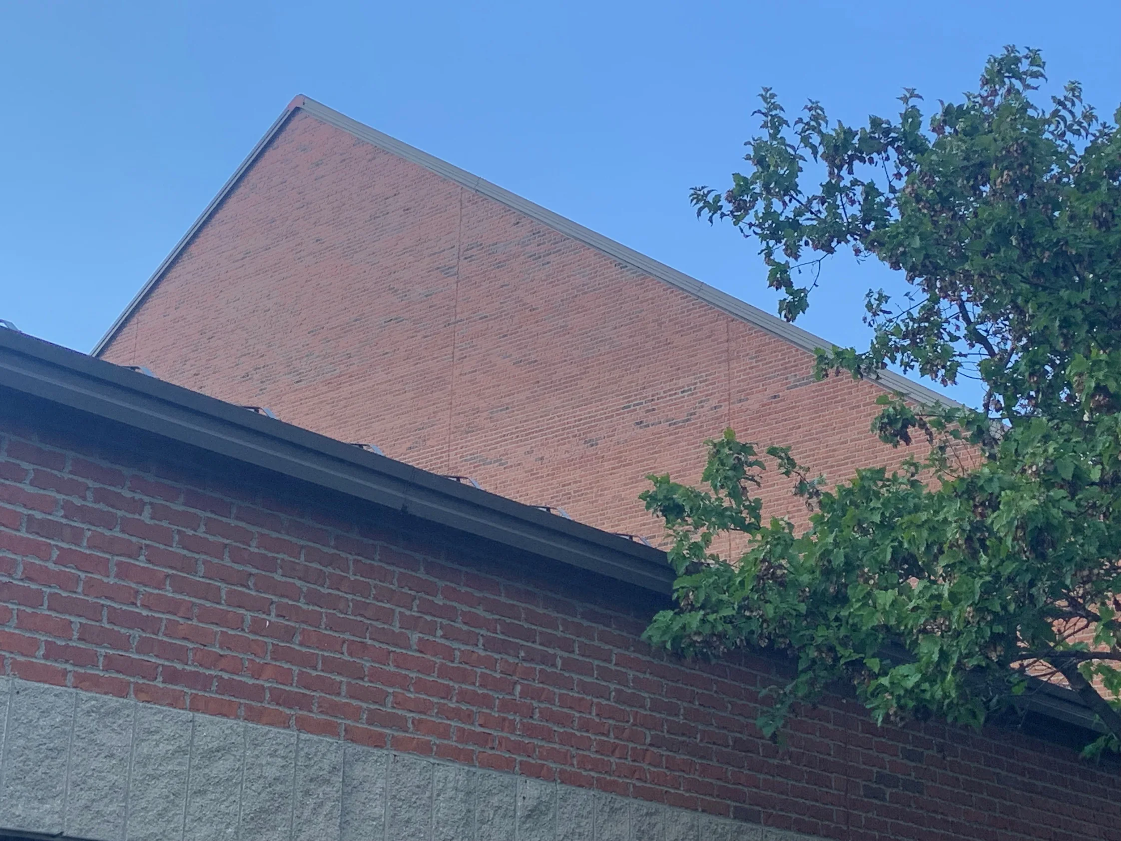 The gable seen from the ground in 2019 against open sky, the stained wall meeting the darker brick and concrete block of the wing in front of it