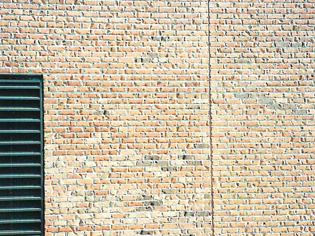 A panel of pale buff brick in 1999, a louvred vent at the left and a vertical control joint running the height of the wall